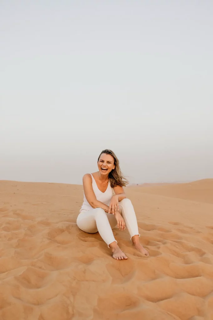 lachende frau, sitzend in der wüste, weißes outfit, fröhlich, fotograf michele peloza